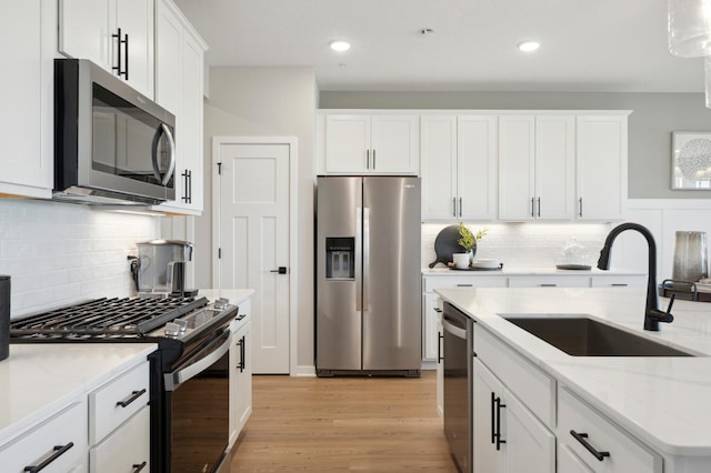 kitchen with stainless steel appliances, decorative light fixtures, light wood-type flooring, white cabinets, and sink