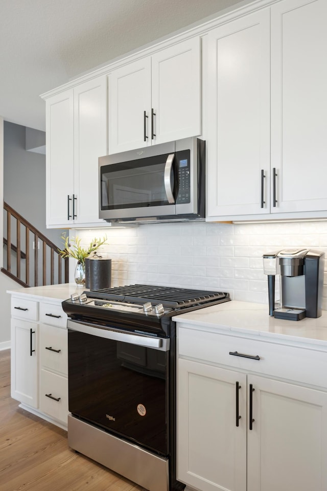 kitchen with tasteful backsplash, white cabinets, stainless steel appliances, and light hardwood / wood-style floors