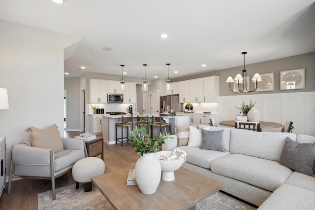 living room featuring light wood-type flooring, sink, and an inviting chandelier