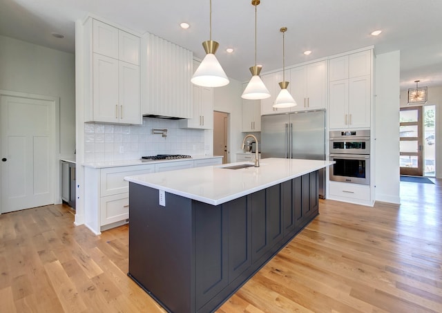 kitchen featuring sink, hanging light fixtures, white cabinets, and an island with sink