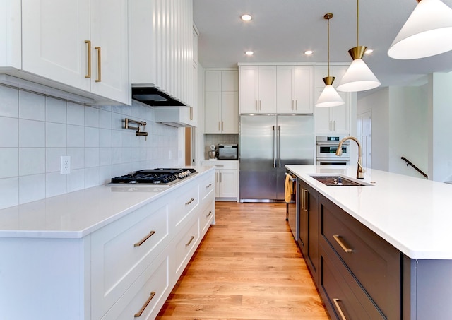 kitchen featuring pendant lighting, sink, white cabinets, a kitchen island with sink, and stainless steel appliances