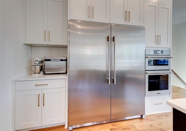 kitchen featuring light hardwood / wood-style floors, white cabinetry, appliances with stainless steel finishes, and decorative backsplash