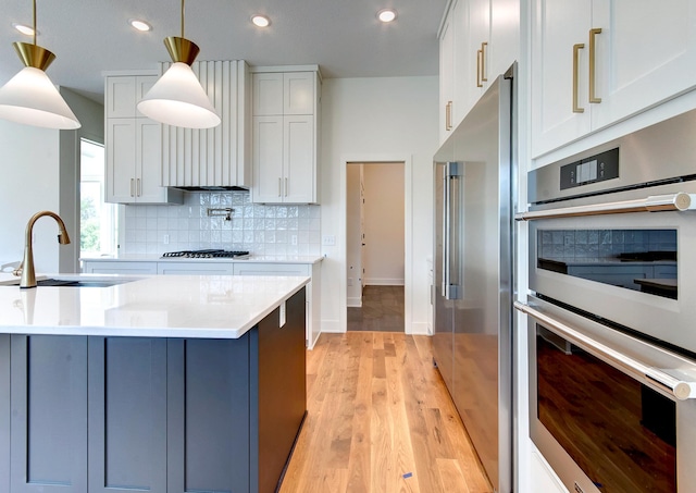 kitchen with appliances with stainless steel finishes, tasteful backsplash, white cabinetry, sink, and decorative light fixtures