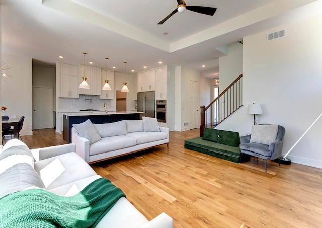 living room featuring ceiling fan, sink, light hardwood / wood-style flooring, and a raised ceiling