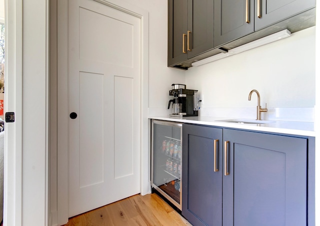 bar featuring sink, beverage cooler, and light hardwood / wood-style flooring