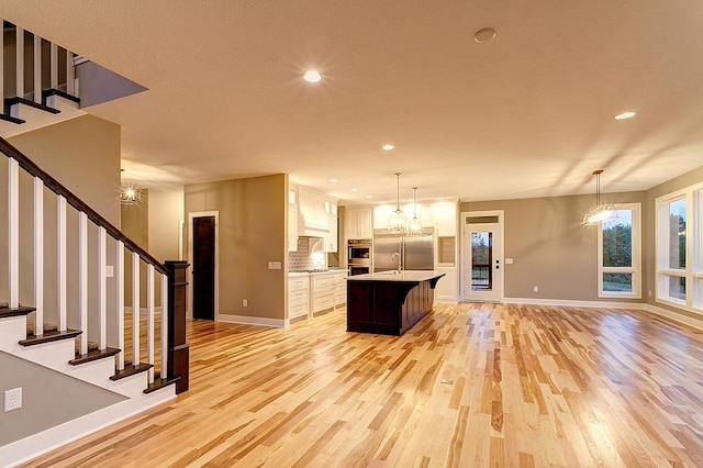 kitchen featuring white cabinets, hanging light fixtures, a center island with sink, and appliances with stainless steel finishes