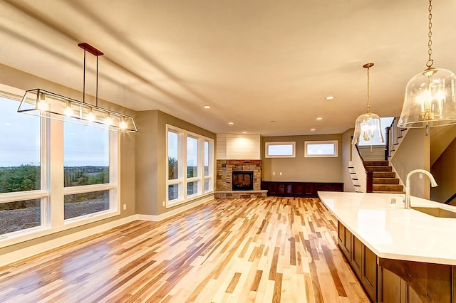 kitchen featuring sink, pendant lighting, a stone fireplace, and light wood-type flooring