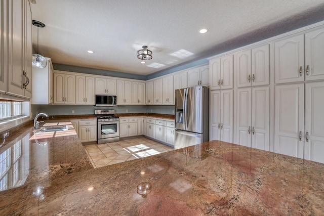 kitchen with dark stone countertops, stainless steel appliances, a sink, and decorative light fixtures