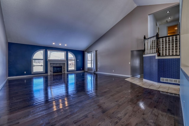 unfurnished living room with high vaulted ceiling, a glass covered fireplace, plenty of natural light, and wood finished floors