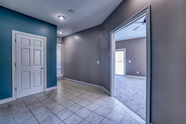 empty room featuring light tile patterned floors, ceiling fan, light carpet, and baseboards