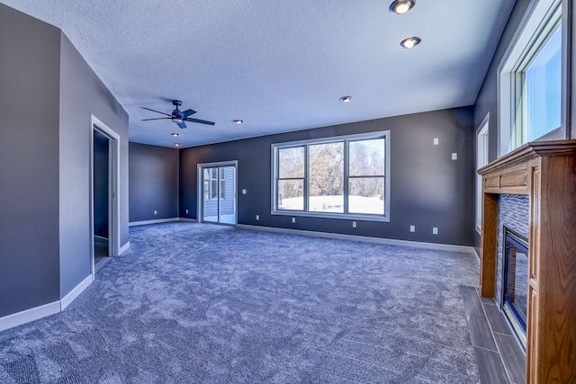 unfurnished living room with a ceiling fan, a glass covered fireplace, a textured ceiling, and baseboards