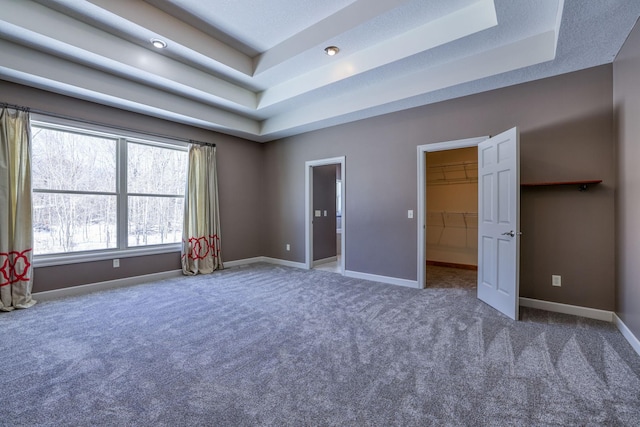 unfurnished bedroom with carpet floors, a tray ceiling, a spacious closet, and baseboards