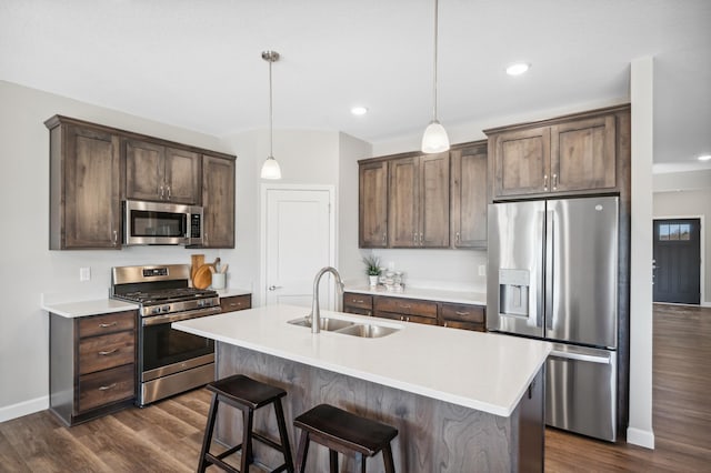 kitchen featuring stainless steel appliances, a kitchen island with sink, dark wood-type flooring, hanging light fixtures, and sink