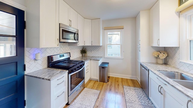 kitchen with light hardwood / wood-style floors, light stone counters, white cabinetry, and stainless steel appliances