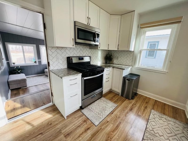 kitchen featuring backsplash, white cabinets, light stone countertops, and stainless steel appliances