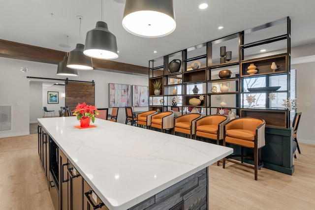 kitchen featuring hanging light fixtures, light wood-type flooring, light stone countertops, a barn door, and a kitchen island