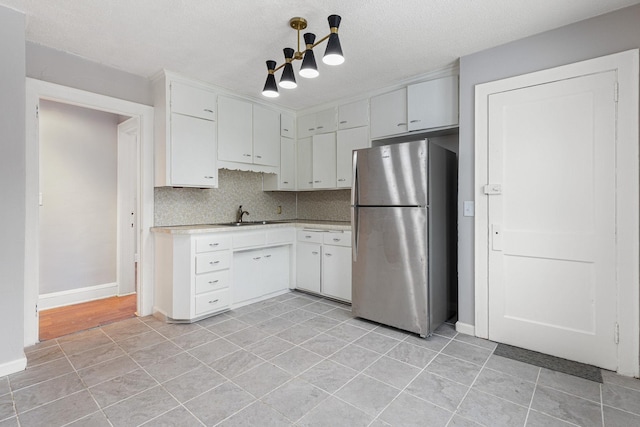 kitchen featuring decorative light fixtures, white cabinetry, sink, backsplash, and stainless steel fridge