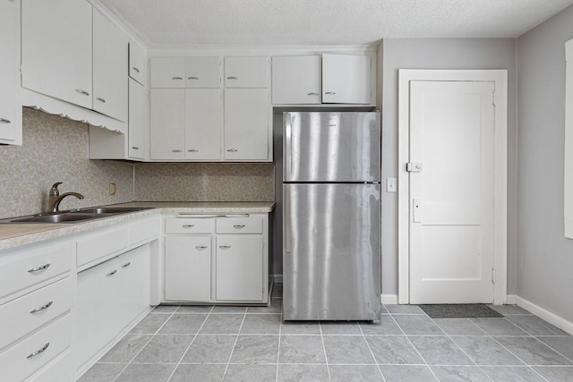 kitchen featuring a textured ceiling, white cabinets, stainless steel fridge, and sink