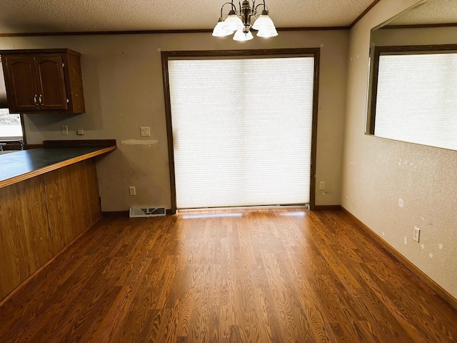 unfurnished dining area featuring crown molding, wood-type flooring, a textured ceiling, and a notable chandelier