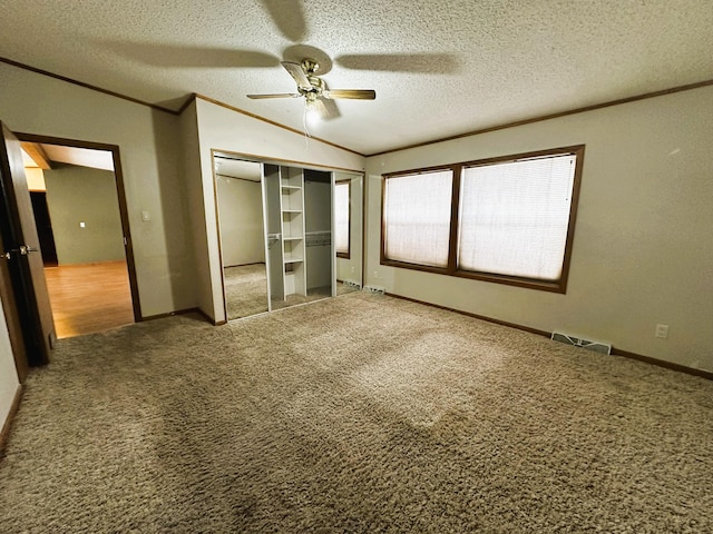 unfurnished bedroom featuring crown molding, vaulted ceiling, a textured ceiling, carpet floors, and ceiling fan