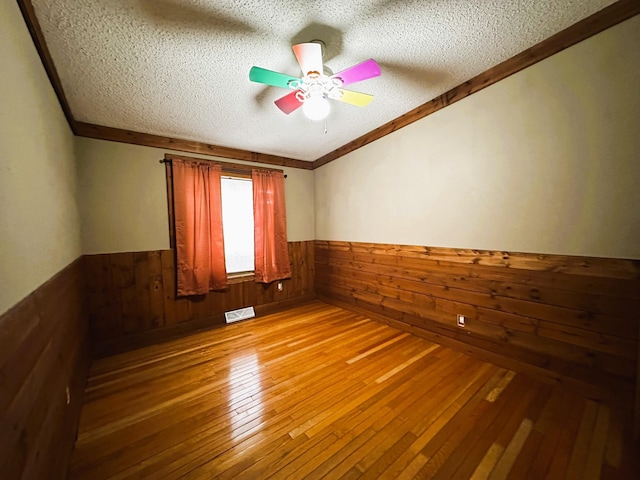 spare room featuring wood walls, crown molding, wood-type flooring, a textured ceiling, and ceiling fan