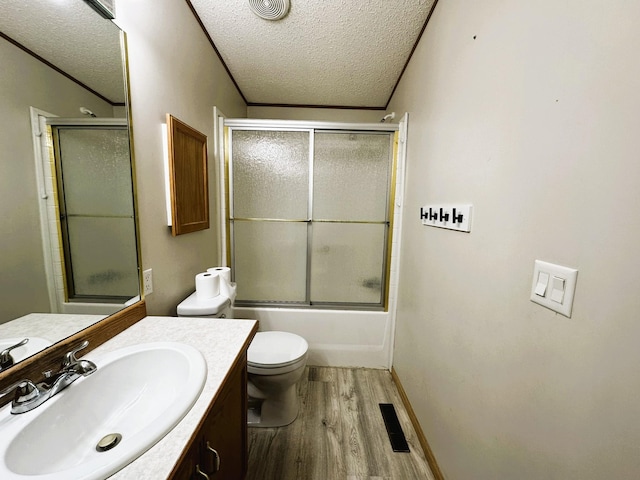 full bathroom featuring combined bath / shower with glass door, wood-type flooring, vanity, toilet, and a textured ceiling