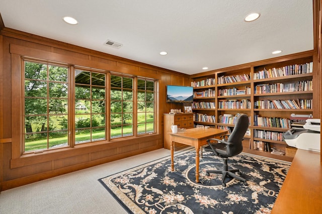 carpeted office space with a textured ceiling, wooden walls, and built in shelves