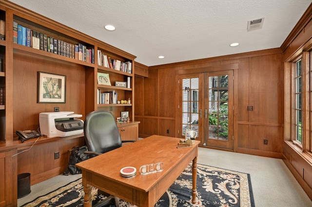 carpeted office space with built in shelves, french doors, wood walls, and a textured ceiling