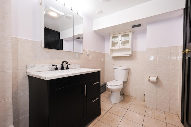 bathroom featuring toilet, vanity, tile patterned flooring, tile walls, and baseboard heating