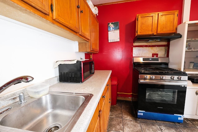 kitchen featuring decorative backsplash, stainless steel gas range oven, sink, and dark tile patterned flooring