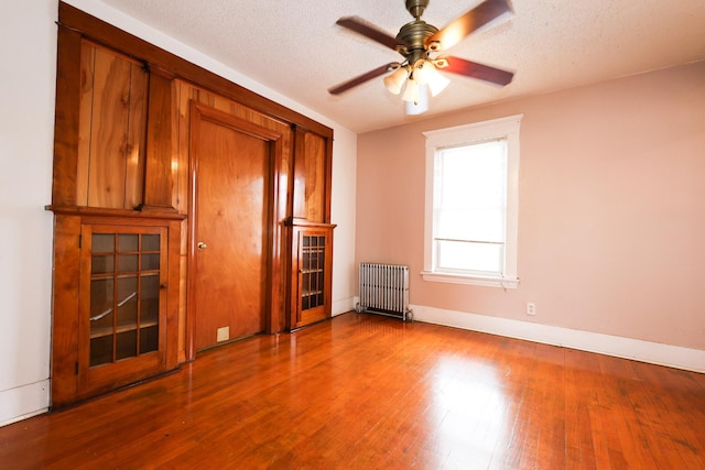 unfurnished living room featuring ceiling fan, radiator, a textured ceiling, and hardwood / wood-style flooring