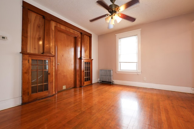 unfurnished living room featuring a textured ceiling, ceiling fan, hardwood / wood-style flooring, and radiator heating unit