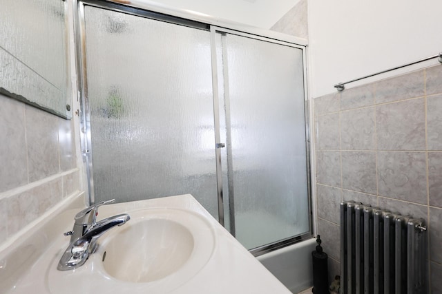 bathroom featuring radiator, combined bath / shower with glass door, and sink