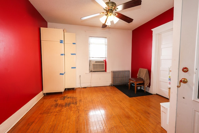 interior space with a textured ceiling, radiator, wood-type flooring, cooling unit, and ceiling fan