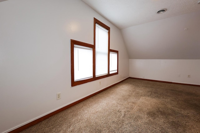 additional living space featuring vaulted ceiling and carpet flooring