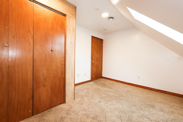 additional living space featuring vaulted ceiling with skylight and light colored carpet