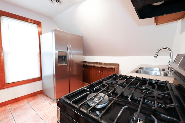 kitchen with light tile patterned flooring, gas stove, sink, stainless steel fridge, and vaulted ceiling