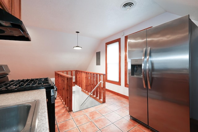 kitchen featuring lofted ceiling, pendant lighting, black gas stove, light tile patterned flooring, and stainless steel fridge