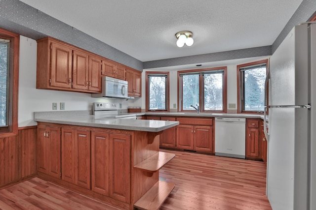 kitchen with light hardwood / wood-style floors, kitchen peninsula, sink, white appliances, and wooden walls