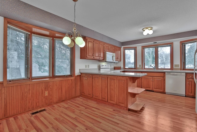 kitchen featuring an inviting chandelier, light hardwood / wood-style floors, kitchen peninsula, white appliances, and hanging light fixtures