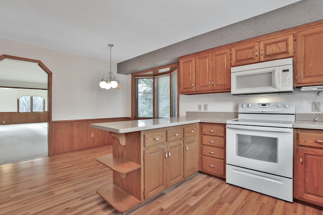 kitchen with wood walls, kitchen peninsula, a notable chandelier, white appliances, and hanging light fixtures