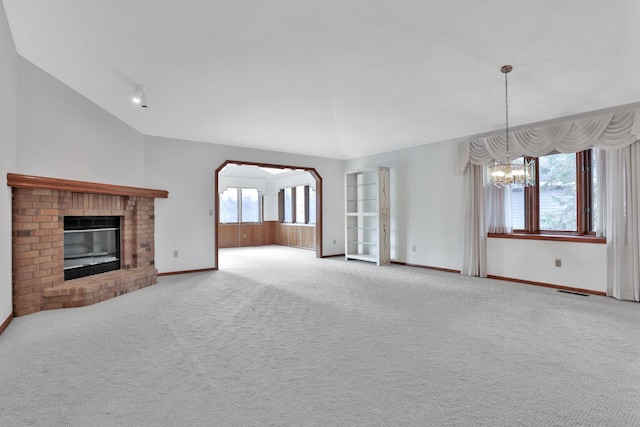 unfurnished living room featuring a brick fireplace, lofted ceiling, plenty of natural light, and an inviting chandelier