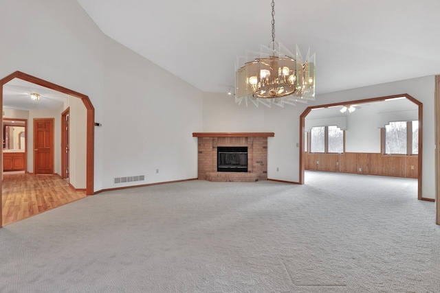 unfurnished living room with a brick fireplace, a chandelier, lofted ceiling, and carpet