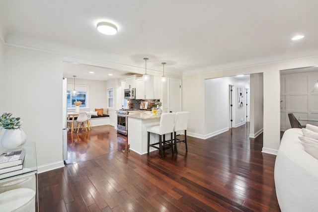 kitchen featuring white cabinets, decorative light fixtures, stainless steel appliances, decorative backsplash, and a breakfast bar area