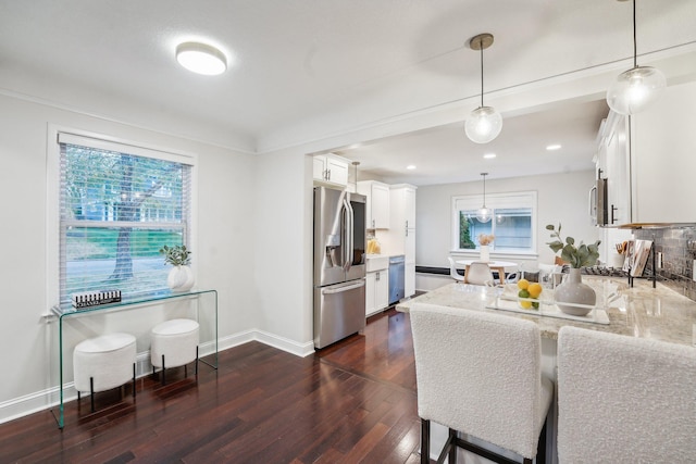 kitchen with white cabinetry, kitchen peninsula, stainless steel appliances, light stone countertops, and pendant lighting