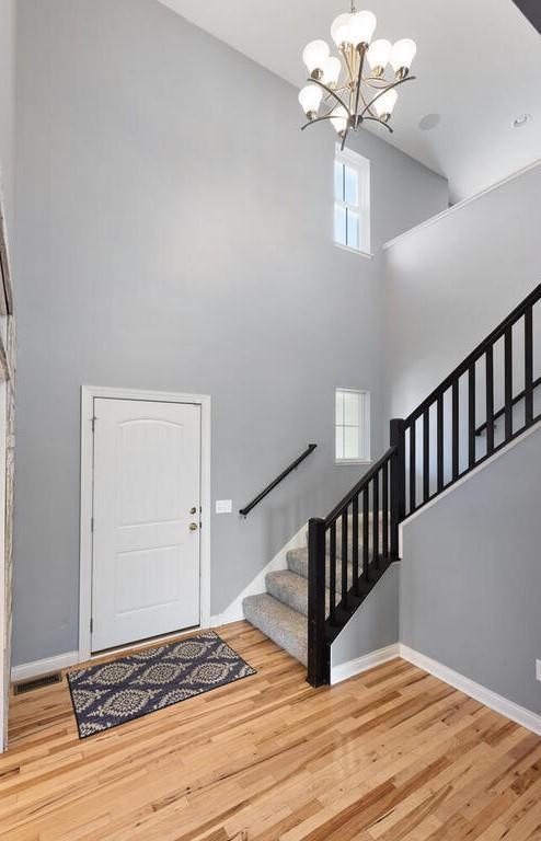 entrance foyer with an inviting chandelier, a wealth of natural light, wood-type flooring, and a high ceiling