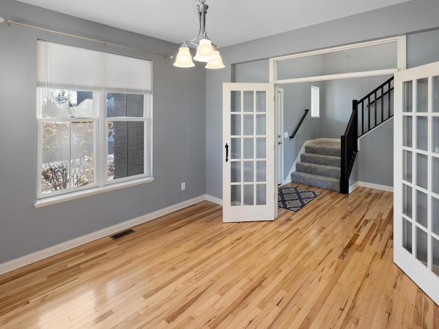 unfurnished dining area featuring french doors, an inviting chandelier, and light wood-type flooring