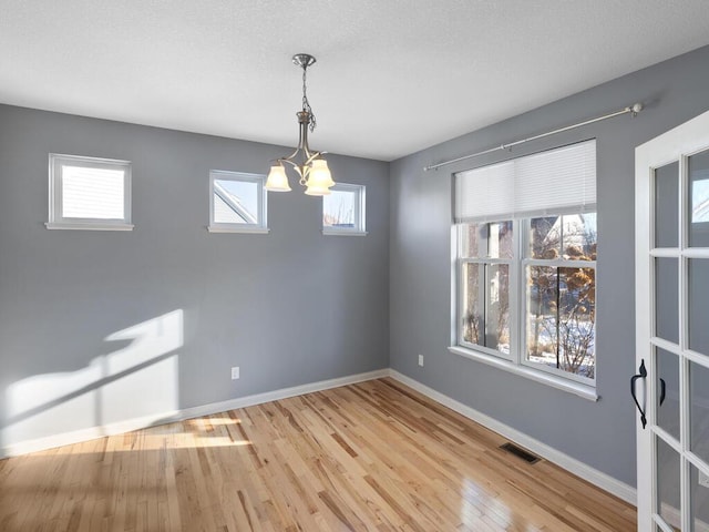 unfurnished dining area featuring an inviting chandelier and light hardwood / wood-style floors