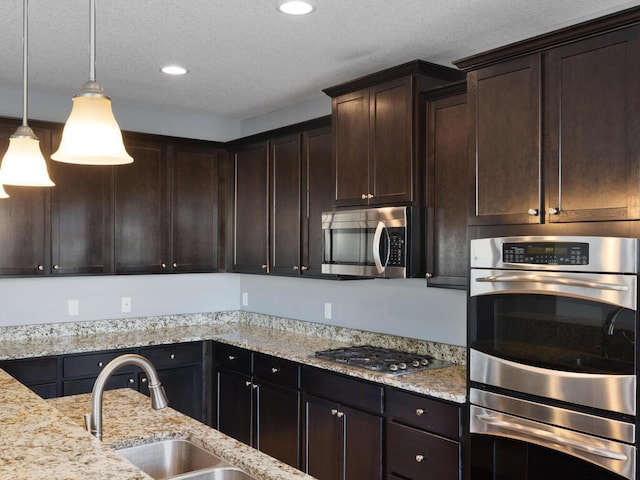 kitchen with dark brown cabinetry, a textured ceiling, appliances with stainless steel finishes, pendant lighting, and light stone countertops