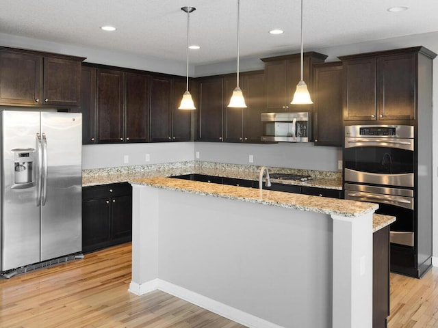 kitchen with pendant lighting, a center island, light hardwood / wood-style floors, stainless steel appliances, and light stone countertops